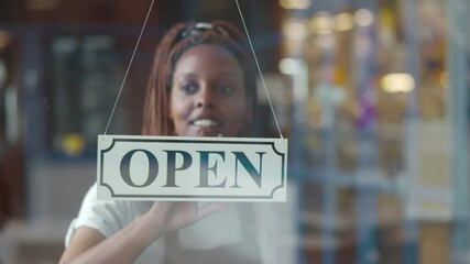 Small business african female owner smiling while turning sign for opening of cafe - Powered by Adobe