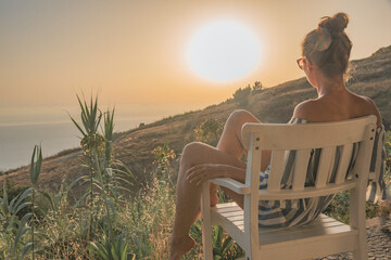 Brunette woman with sunglasses sitting on a white chair looking in the sunset