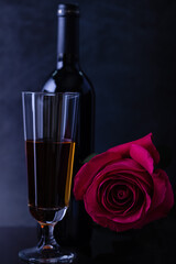 A bottle of wine with a beautiful glass and a beautiful rose on a dark background.
