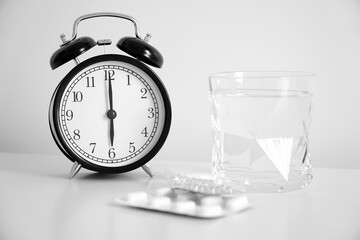 Pills, healthcare and medical concept. An image of a retro clock showing 6:00 am. Water in clear glass, medicine in morning time.  Wake up concept, healthy lifestyle.