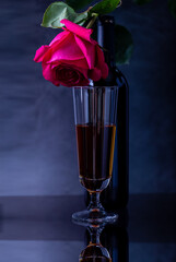 A bottle of wine with a beautiful glass and a beautiful rose on a dark background.