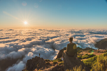 Woman on top of a summit watching the sunrise over the fluffy clouds	

