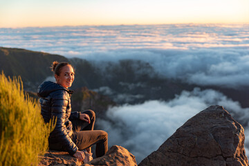 Woman on top of a summit watching the sunrise over the fluffy clouds	
