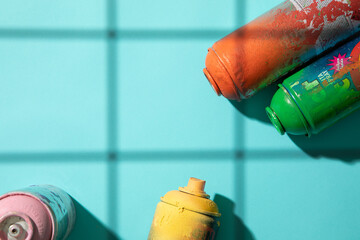 Another top view of used spray paint cans on cyan background with grid shadows and free space for...