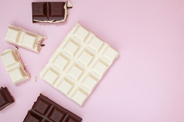 White and black chocolate bars and pieces on pink background, top view