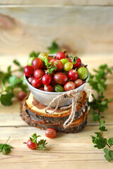 Selective focus. Macro. Gooseberries in a bowl on a wooden surface. Gooseberry leaves and branches. Harvest gooseberries. Rustic style.