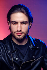 A young man of 25-30 years in in a leather jacket emotionally poses on a purple background. 