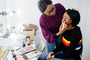 African American woman applying make-up by make-up artist at beauty saloon.