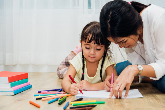 Happy Asian child kid daughter kindergarten and young beautiful parent mother teaching drawing and play color together at interior room home, family day and Back to school concept