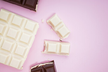 White and black chocolate bars and pieces on pink background, top view