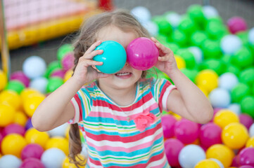 Little cute girl plays in bright colored plastic balls, a child's leisure.
