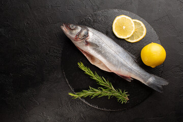 Raw sea bass with fresh rosemary and lemon on stone plate on black concrete background.Top vie,copy space.