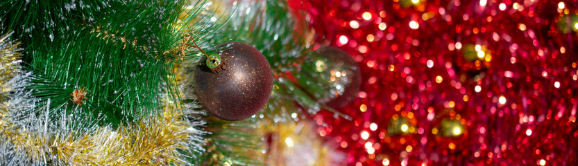 Christmas banner: a brown and gold Christmas ball weighs on a branch of a Christmas tree against a background of red tinsel and Golden balls. The view from the top, place for text. © Leila