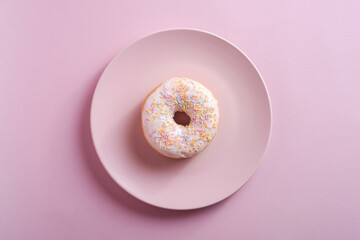 Vanilla donut with sprinkles on pink plate, sweet glazed dessert food on pink minimal background,...