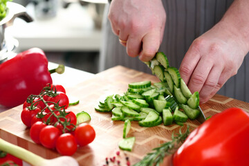 Close up of cook slicing a cucumber on a chopping board while cooking in the kitchen. Healthy homemade food concept