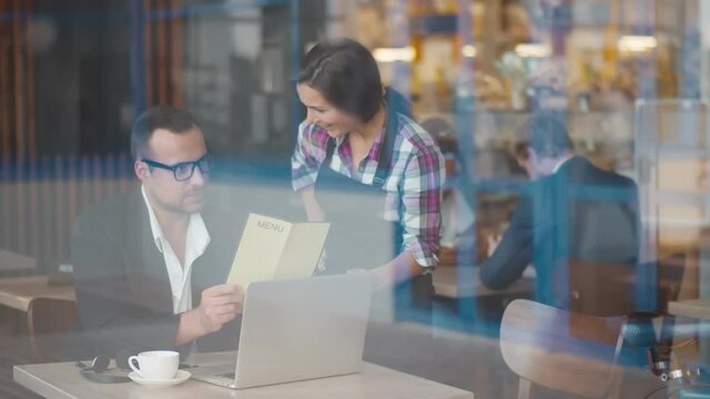 Young waitress recommending businessman dish from menu in cafe