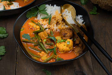 Vegan Thai red curry with seitan, beans and cauliflower over rice, served in black bowls