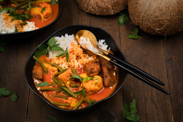 Vegan Thai red curry with seitan, beans and cauliflower over rice, served in black bowls, copy space
