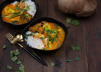 Vegan Thai red curry with seitan, beans and cauliflower over rice, served in black bowls, copy space