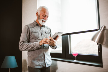 Smiling senior man reading news on digital tablet. Cheerful excited mature male using portable computer at home