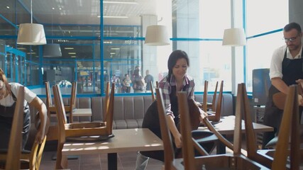 Cheerful multiethnic cafe workers arranging chairs preparing for work in morning