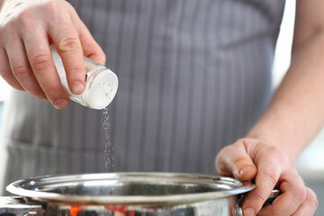 Close up of man wearing apron and using salt to make soup in the kitchen. Healthy homemade food concept
