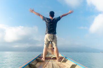 Asian traveler man standing and raising his hands in the air on boat,Freedom concept.