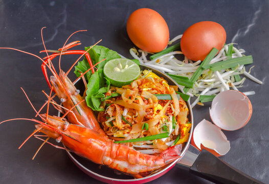 Well known street food thai cuisine "Pad thai" stir fried noodles with River Prawns Serve in small red pan.
