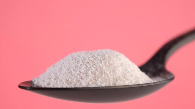 pouring collagen powder in black spoon, pink background closeup. Natural beauty and health supplement