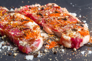 Fresh rare  striploin beef portion with seasoning , herb and spice prepared for cookingon  black stone background.