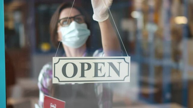 Waitress in medical mask replacing open sign with quarantine sign on cafeteria door.