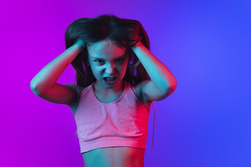 Angry, crazy looks. Little girl's portrait isolated on gradient pink-blue studio background in...