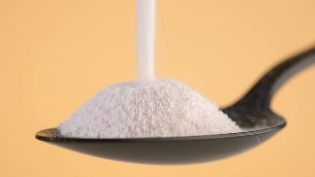 pouring collagen powder in black spoon, yellow background. Natural beauty and health supplement