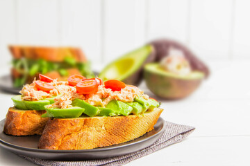 sandwich with fish tomato and avocado on top of a black plate. Healthy food