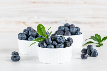 Fresh ripe blueberries in white bowls on white wooden background close up. Farmer’s food. Healthy summer dessert on the table.