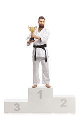 Full length portrait of a karate champion in kimono with a trophy cup on a winners podium