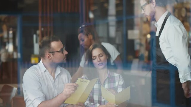 Cheerful couple with menu in a restaurant making order to young waiter