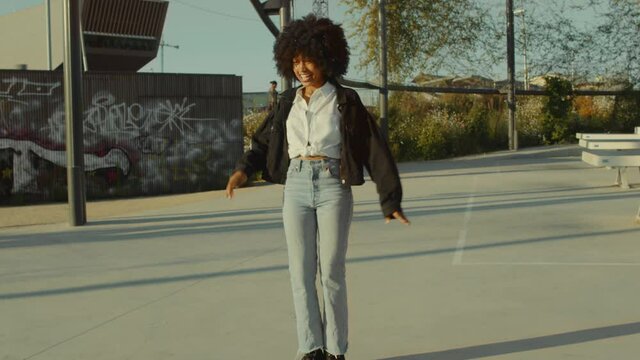 Black woman with huge afro hair and disco-style clothes look Dancing outdoors in tennis park zone in morning light