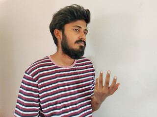 Sad Indian beard man, showing helpless gesture with arm and hands, mouth curved as if he does not know what to do. Isolated on white background. Stripped t-shirt