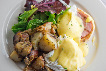 Eggs Benedict. Traditional classical American diner or French Bistro brunch item. Homemade Hollandaise sauce drizzled over a poached egg, country ham on top of a toasted English muffin with avocado.