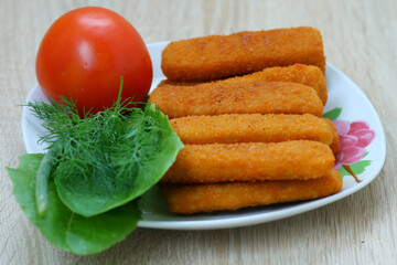 Delicious fried fish sticks with tomato and greens in a beautiful plate