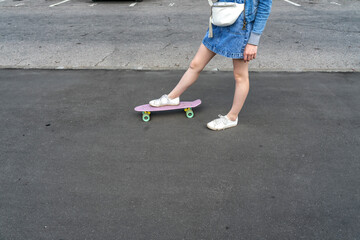 close-up legs of a young girl on a skateboard in sneakers and a denim skirt on the road