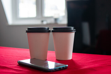 Photo of a red table with two coffe to go cups and a phone.