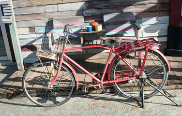 Fototapeta na wymiar The red bicycle has a wooden backdrop and is exposed to sunlight and has a shadow.
