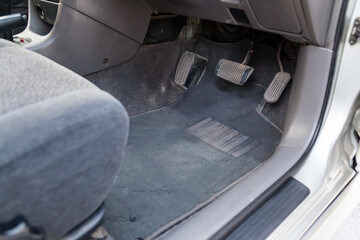Gray cloth car mat in the interior of a Japanese sedan with three pedals gas, brake and clutch in a...