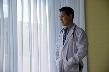 Portrait of Asian male Doctor in medic uniform with stethoscope standing post in Hospital office