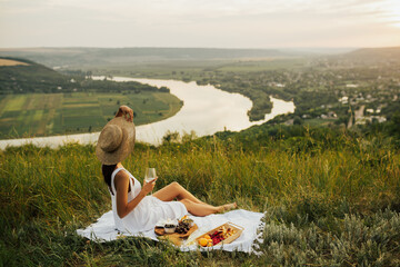 Woman in white dress with straw hat with glass of wine, raspberries, croissants, brie cheese,...