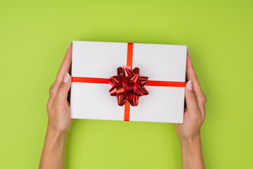 Top view of female hands holding a present box package in palms, on green background