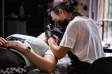 Obraz na płótnie Canvas Girl artist paints an eyebrow tattoo. The process of tattooing. Permanent makeup