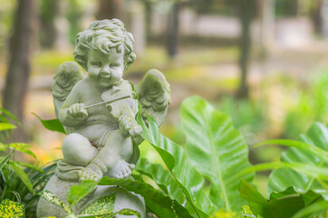 Obraz premium Figurine of a little angel cupid playing the violin in the garden.